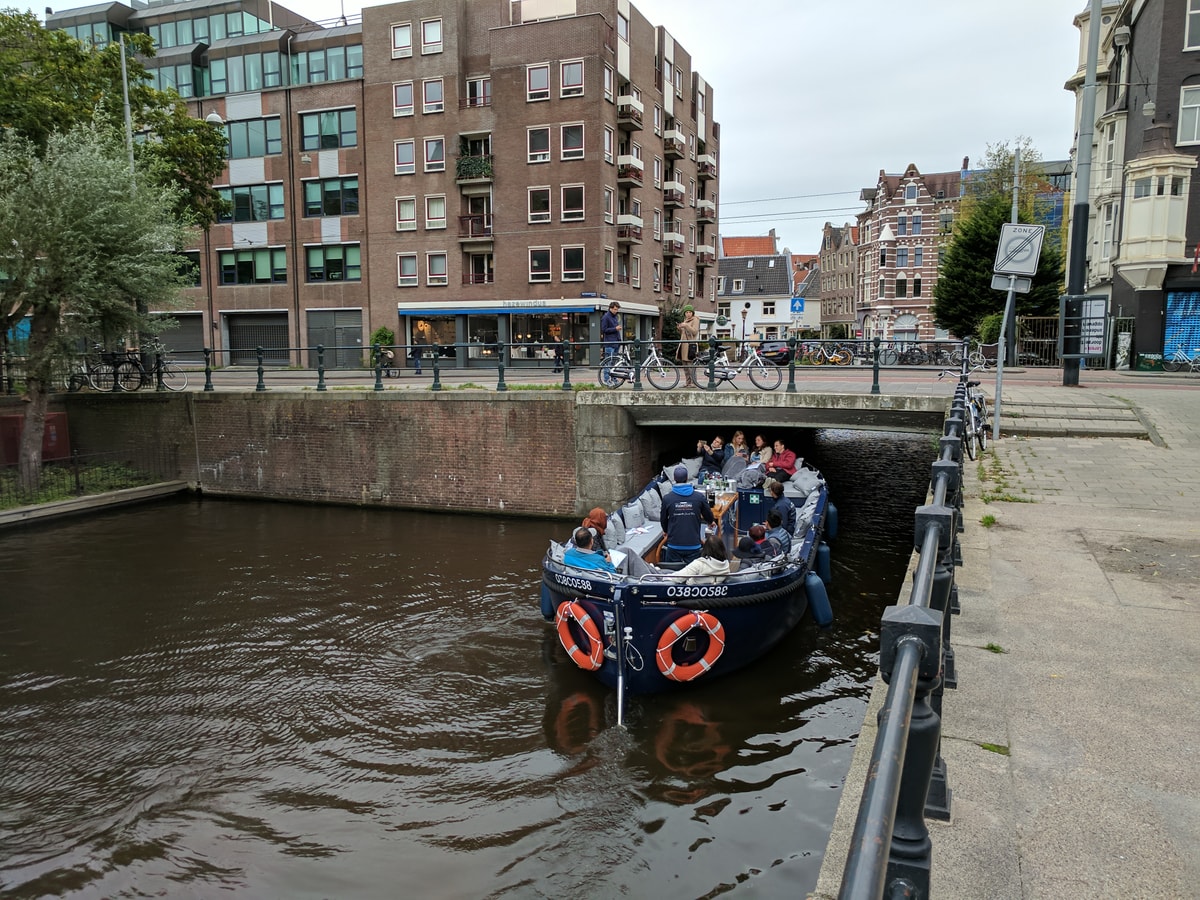 A party boat goes under the bridge. Everyone is sitting down to avoid hitting their head.