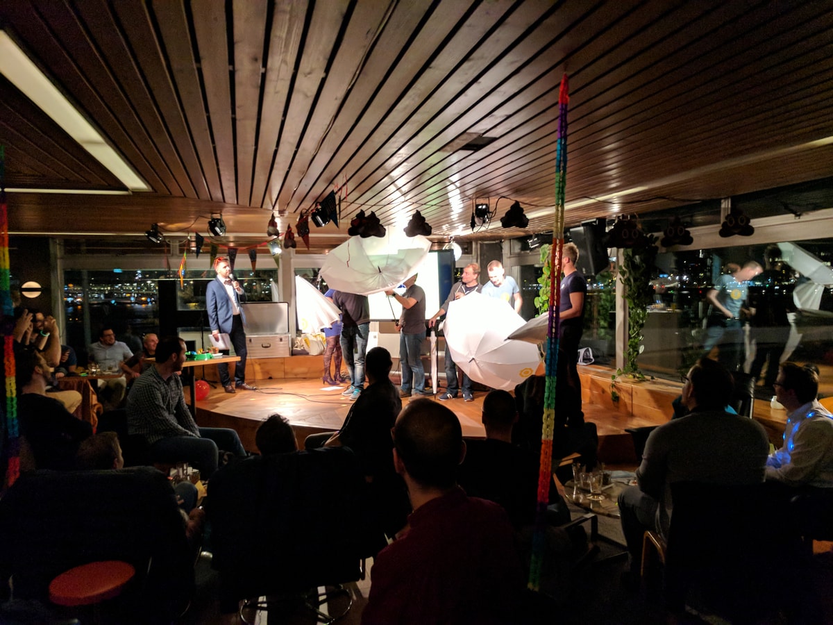 A bunch of men on a small stage playing with umbrellas. One has turned inside out.