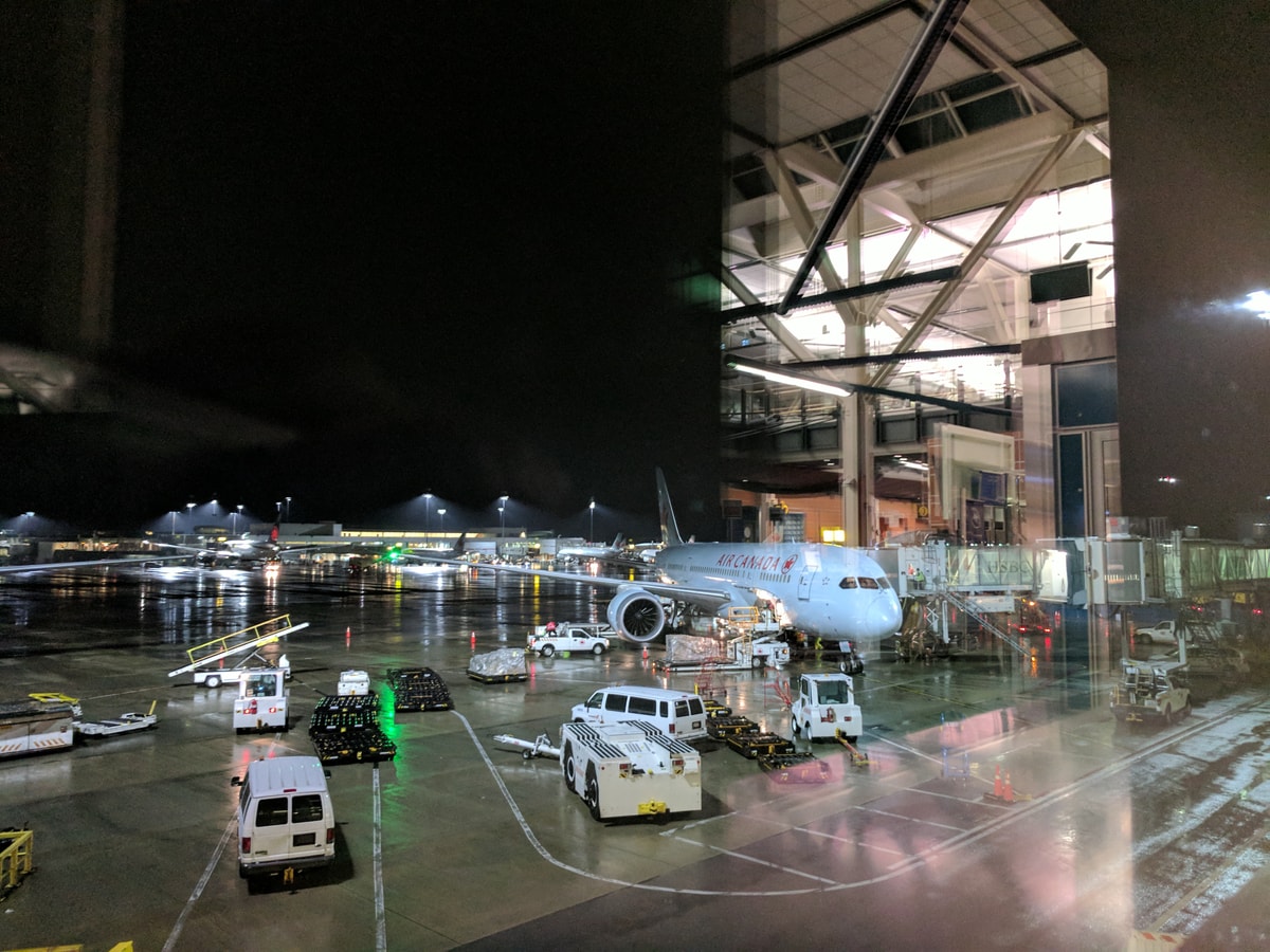 At the airport at night, there's a CanadaAir plane waiting and a whole host of vehicles scurrying around the tarmac.