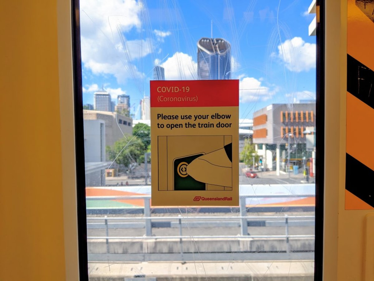 Looking out the train window. Brisbane City in the background. Sticker on the window: "Please use your elbow to open the train door"