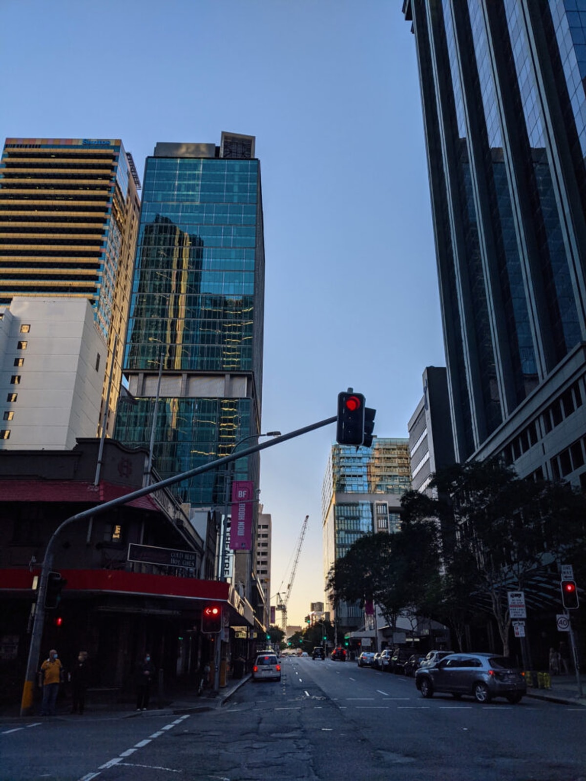 Looking down George Street. The road is super damaged, and the skyscrapers form an urban canyon. There's a glimpse of sunset on the horizon.