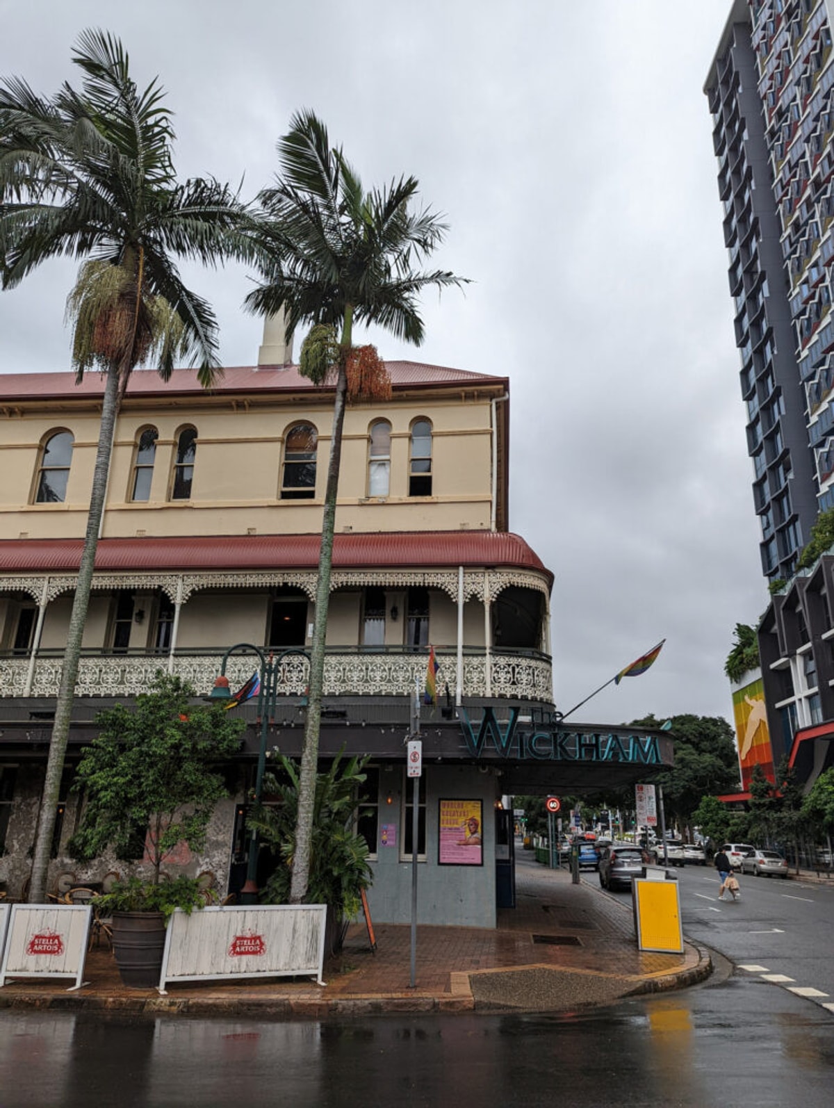 The exterior of The Wickham Hotel, a three story pub with palm trees out the front. It's overcast.