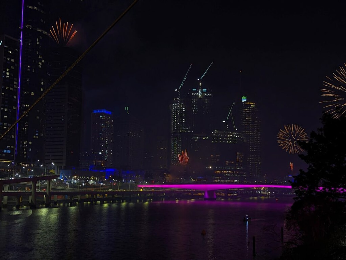 Fireworks over a smoky Brisbane City, with the Victoria Bridge lit up Brisbane Festival Pink.