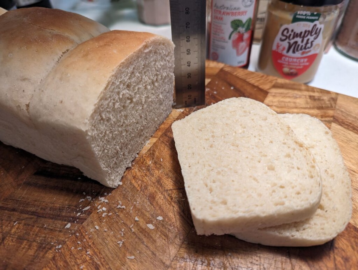 Two slices of bread are cut off. It's a fairly good crumb, with an even texture. It's about 70 cm high, and there's peanut butter and jam in the background. 